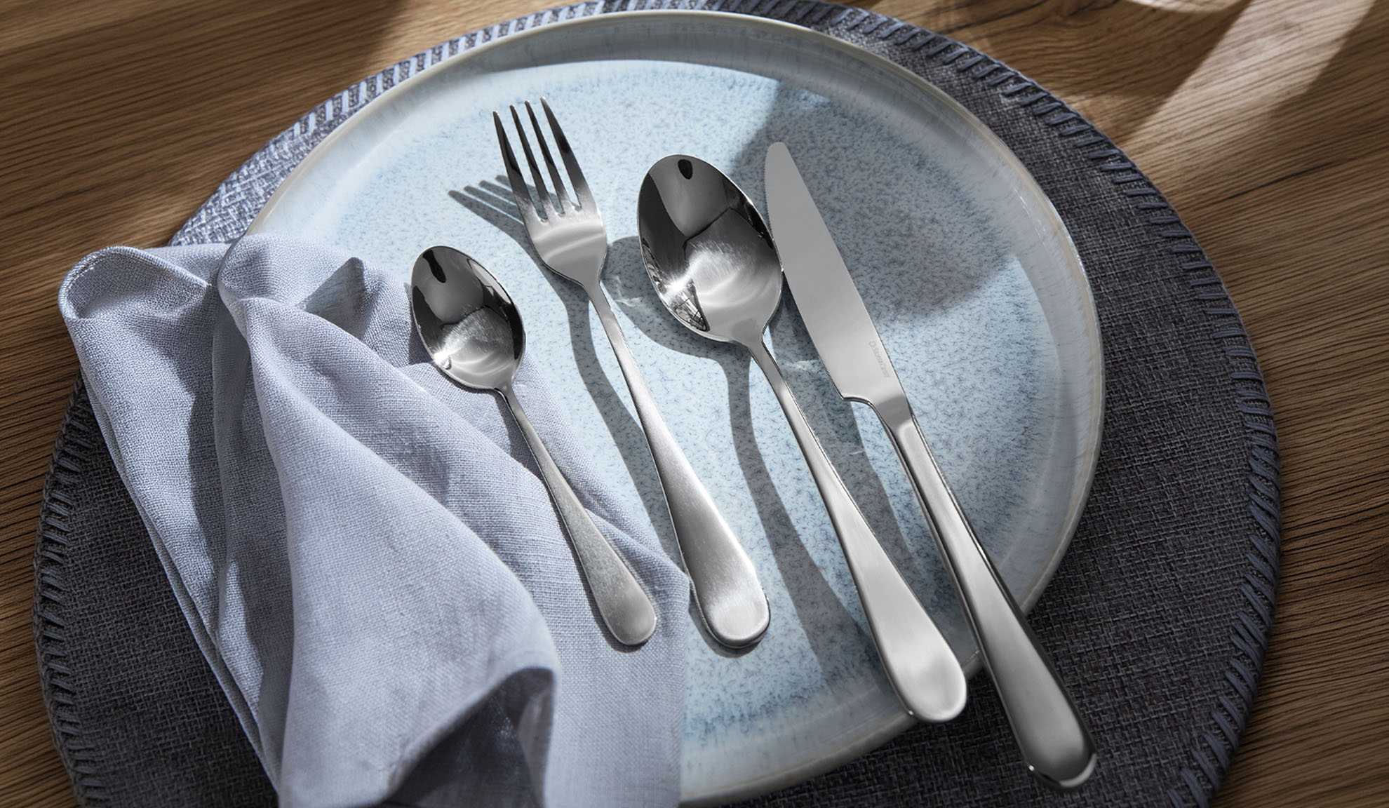 Silver cutlery on a blue plate, with a napkin and placemat.