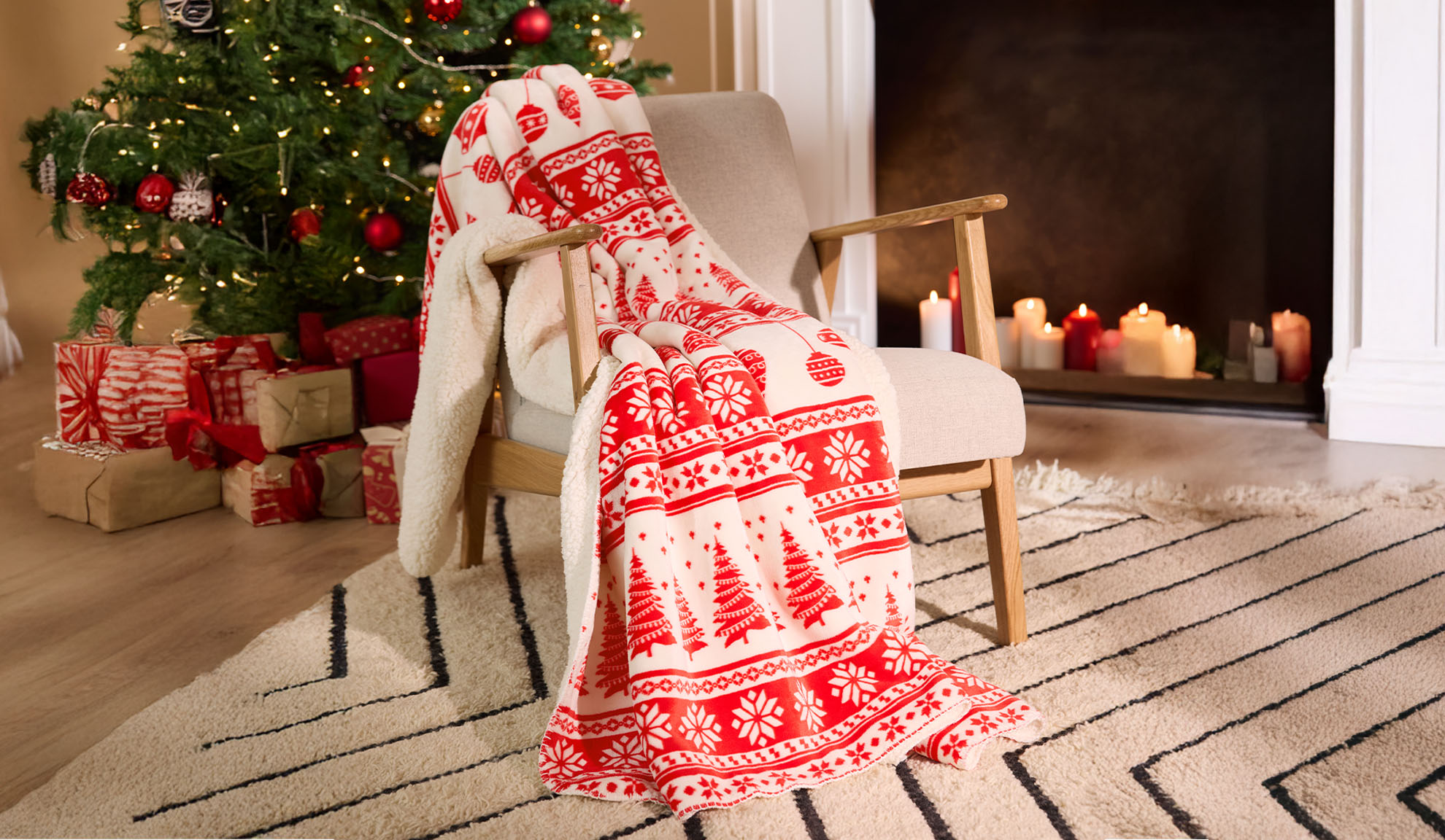 Red and white Christmas blanket on an armchair next to an illuminated Christmas tree and gifts.