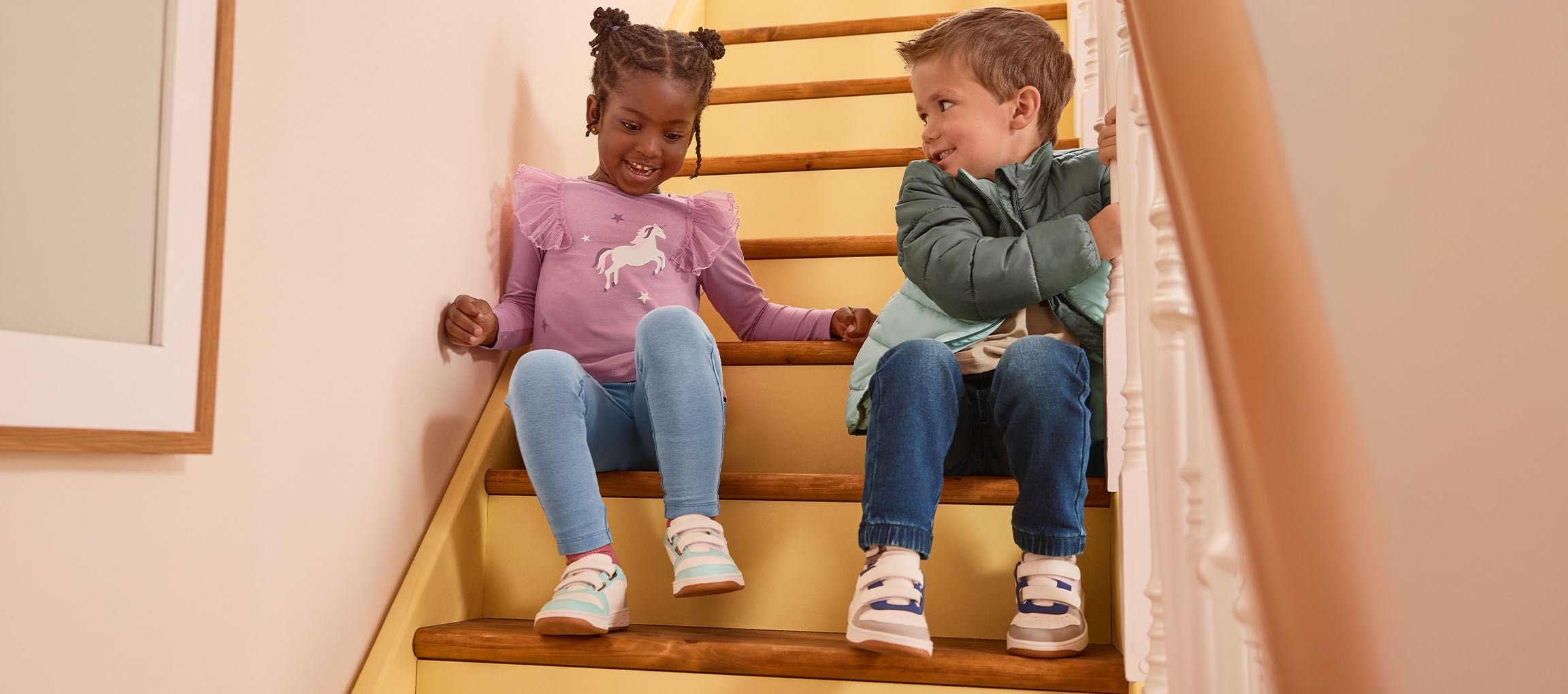 Two children sitting on stairs, a girl in a purple shirt and a boy in a green jacket.