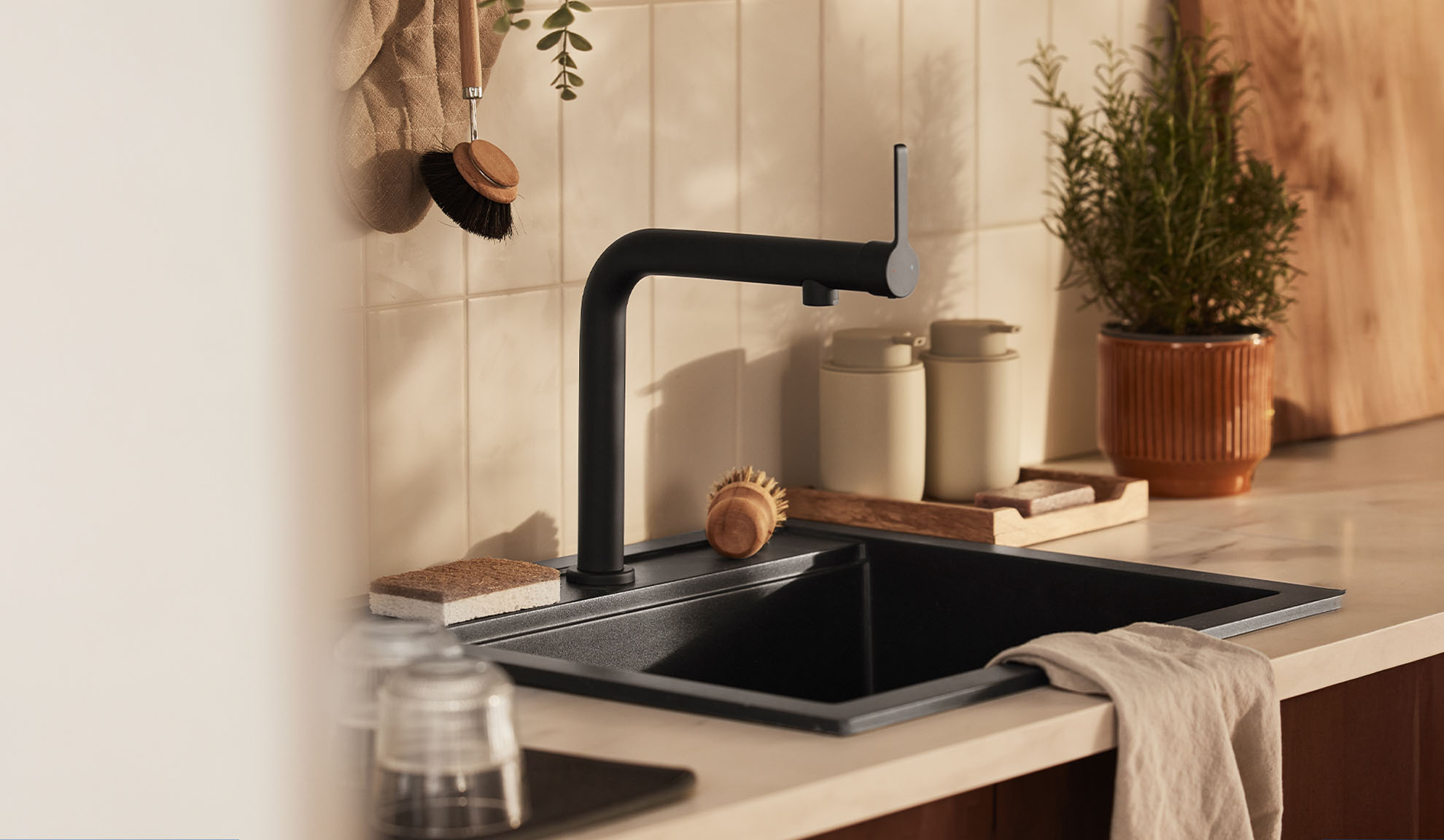 Modern kitchen sink with black faucet, cleaning brushes, and herbs.