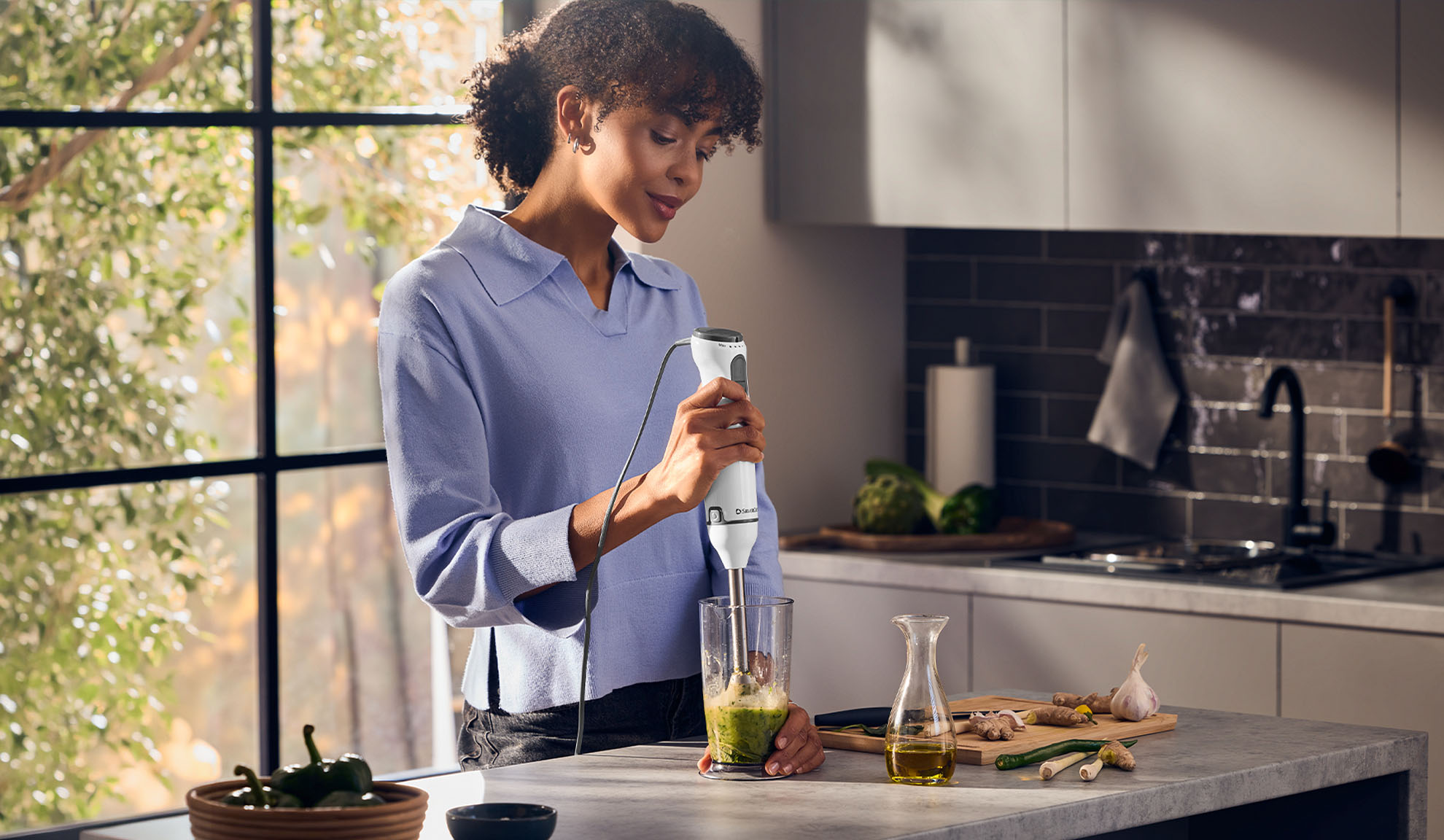 Woman in a kitchen using a hand blender to make a green smoothie.