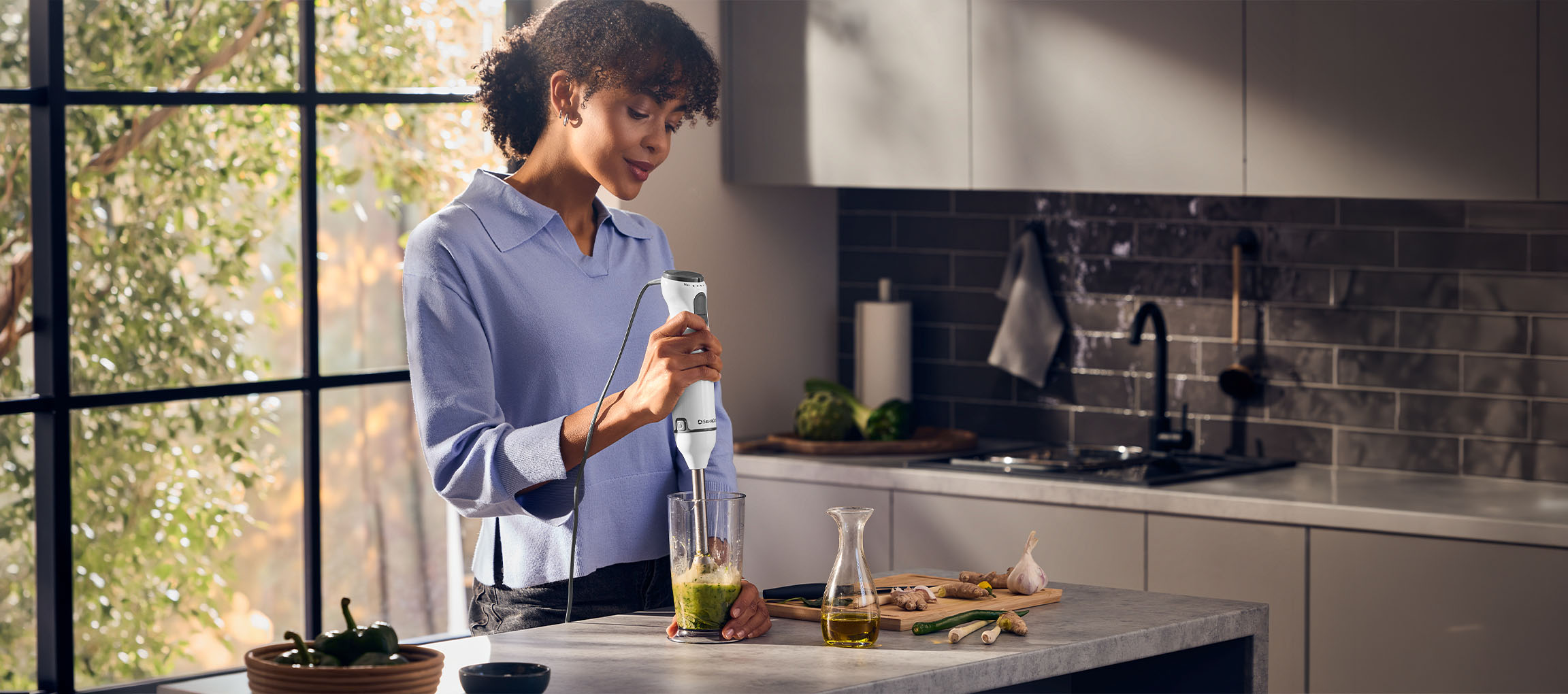 Woman in kitchen using a hand blender to make a green smoothie.