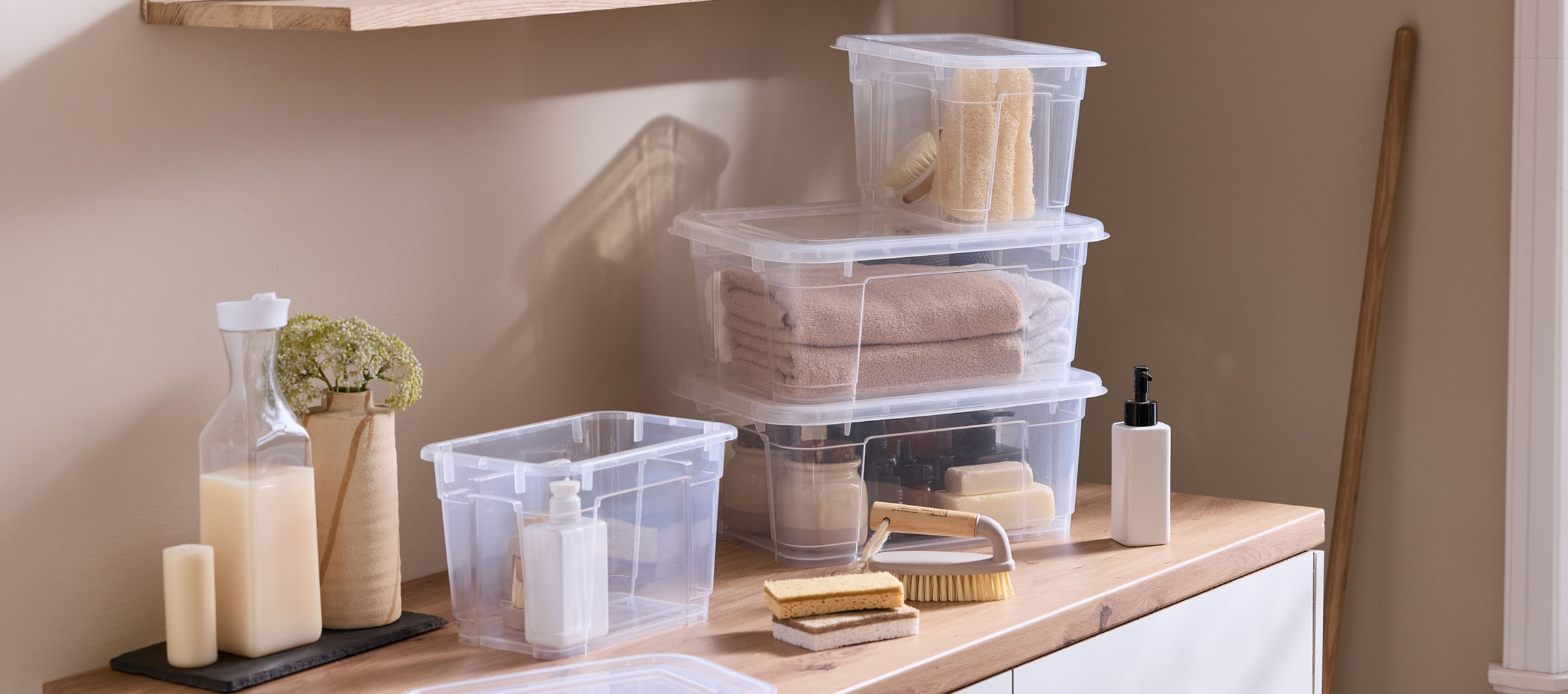 Clear plastic boxes with towels and bath essentials on a wooden countertop.