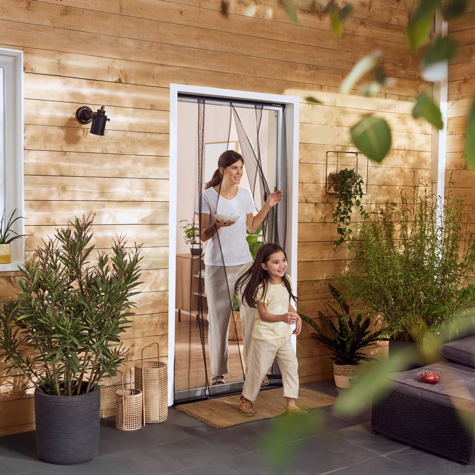 Woman and girl stepping onto a patio with plants through an insect screen.