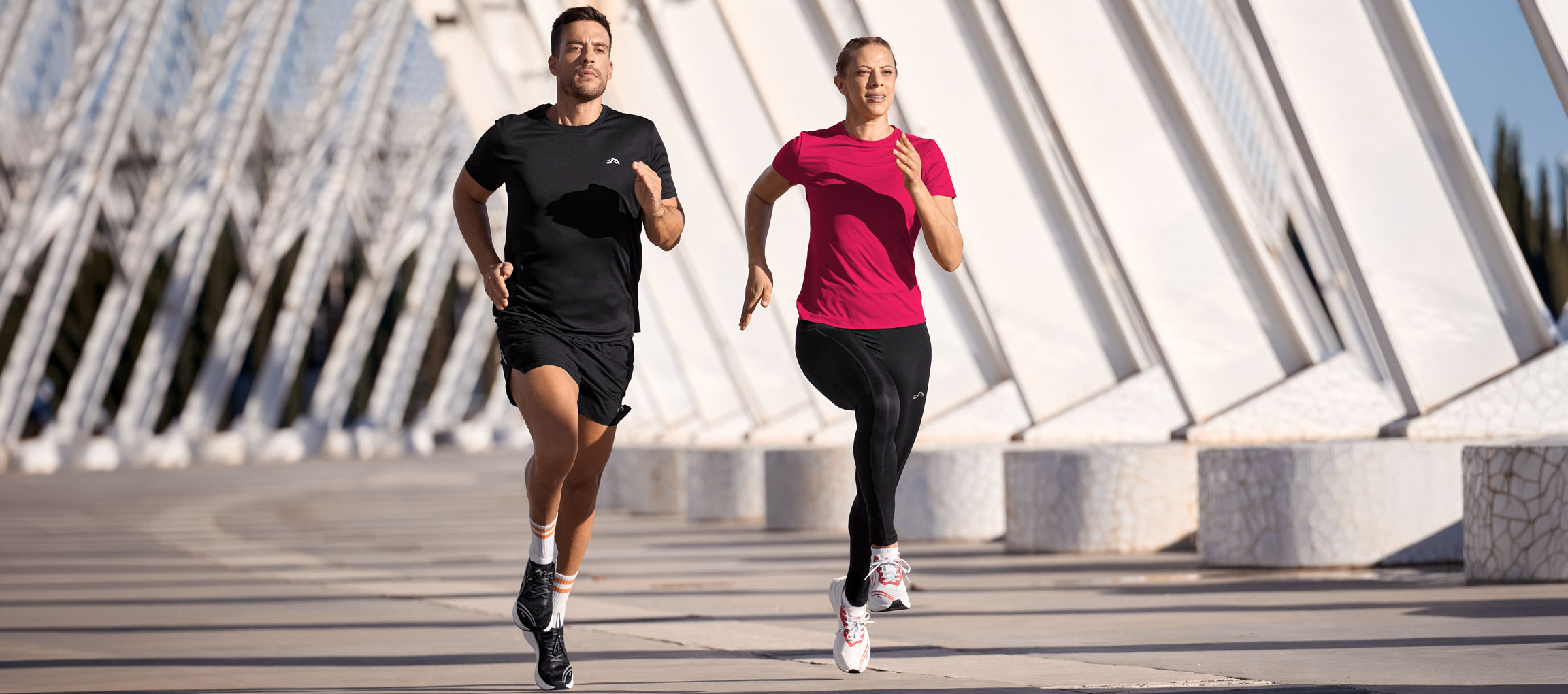 Man and woman running in athletic wear, black and pink tops, black shorts and leggings.