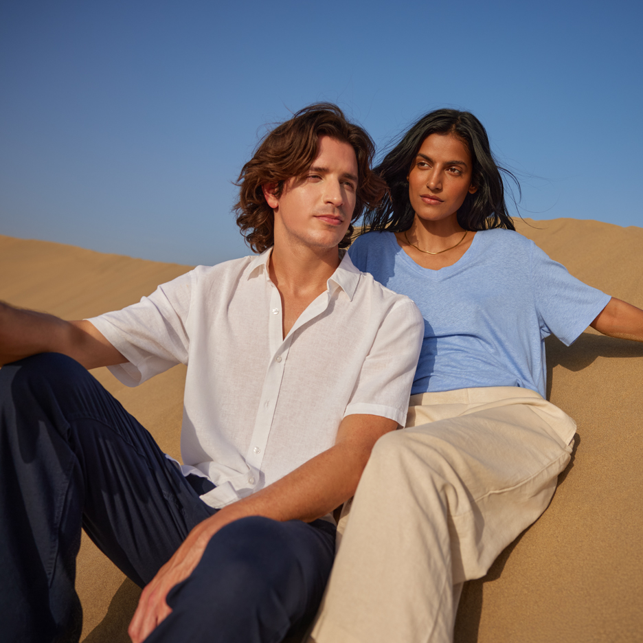 Two young people in the desert, wearing a white shirt and blue t-shirt, navy and beige trousers.