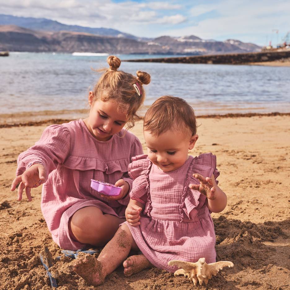 Two girls in pink dresses playing in the sand at the beach.