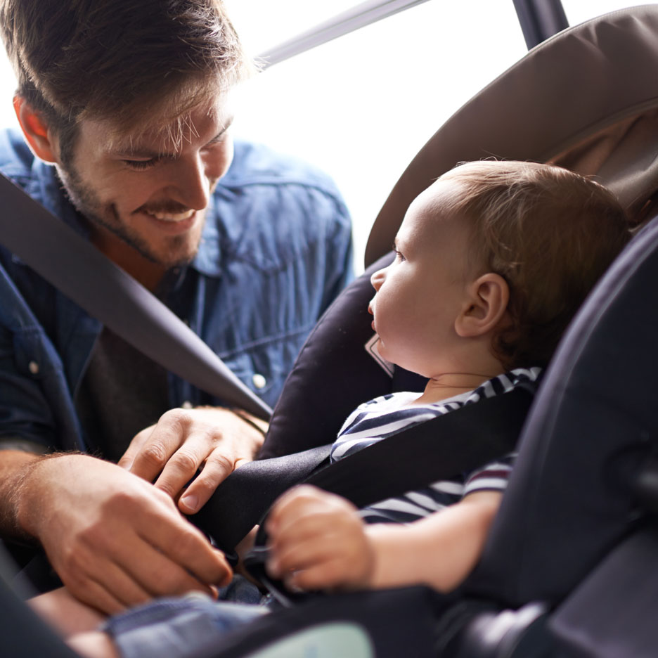 A father secures his baby in a car seat.