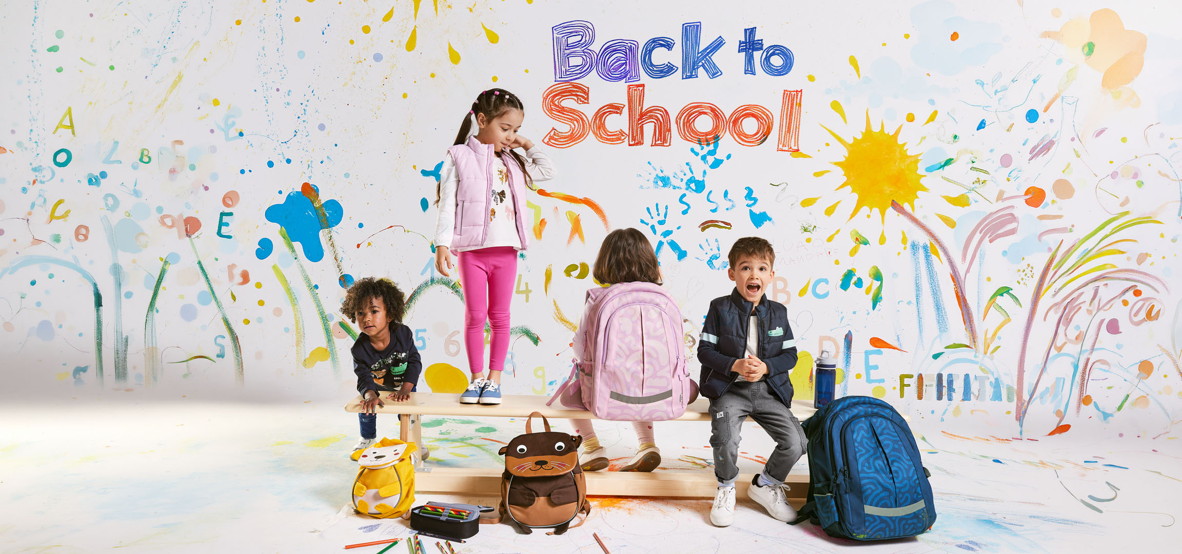 Children with backpacks and school supplies against a background of colorful drawings with