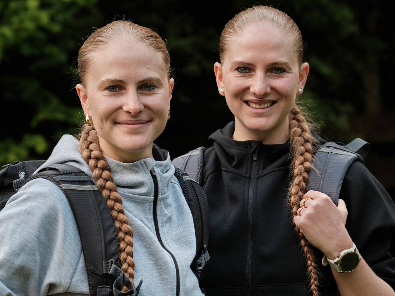Two women with backpacks stand together.