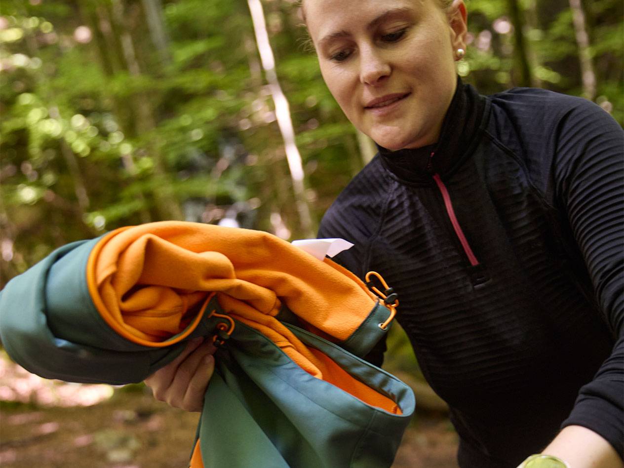 Woman in a forest folding a sports jacket.