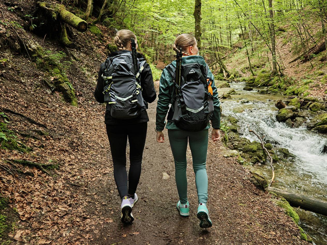 Two women with Crivit backpacks hike a forest trail.